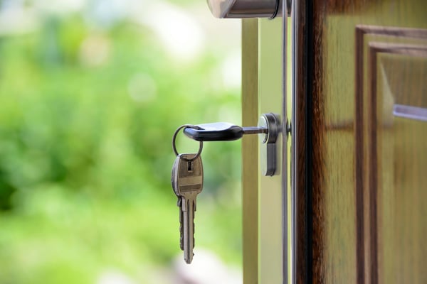 Key in lock of wooden door with green garden visible through blurred background