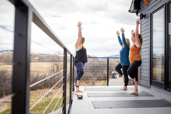 Three women doing yoga on a deck with mountain and valley views in the background
